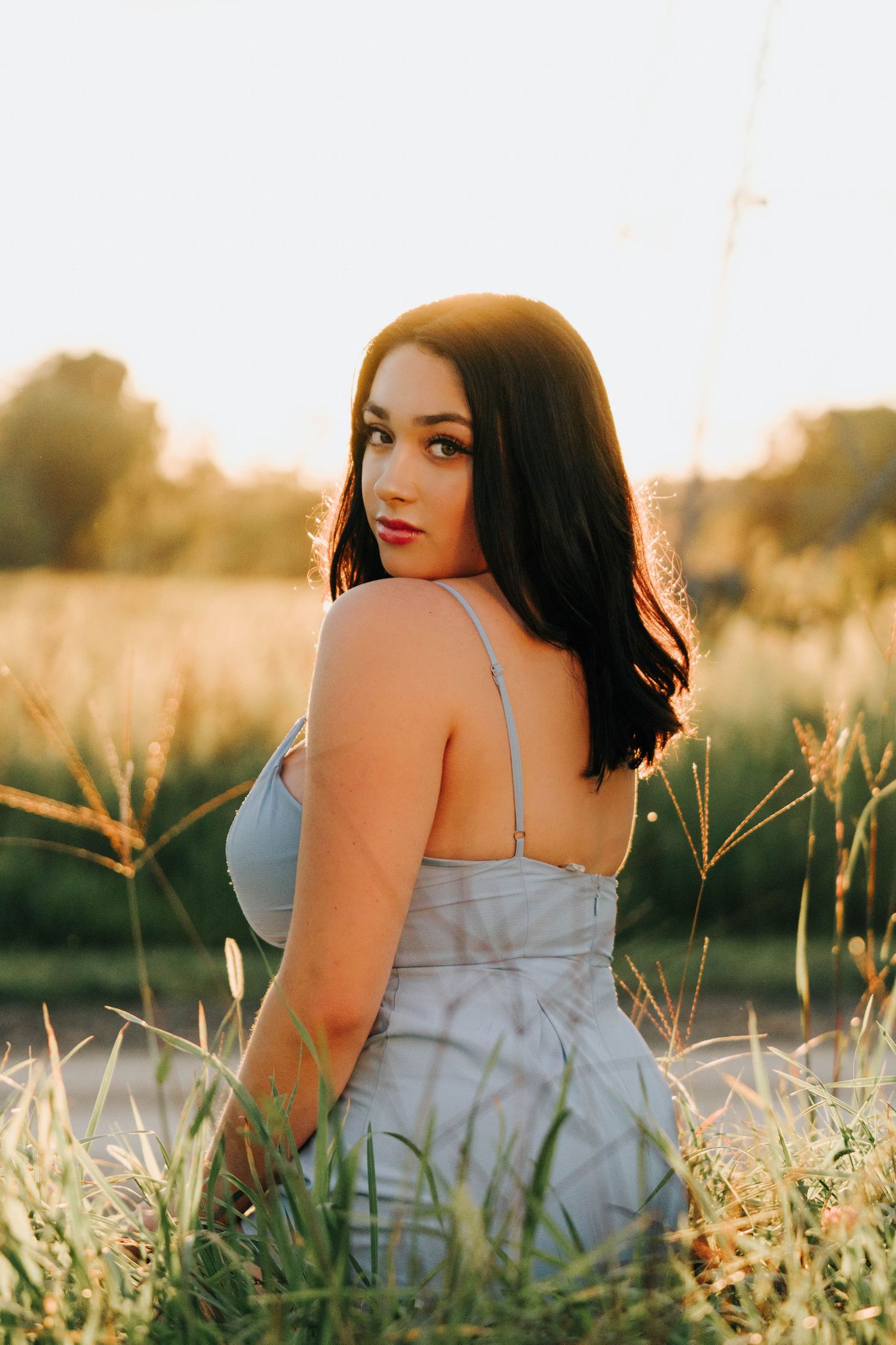 Person in light dress reclining in golden sunset light among tall grass.