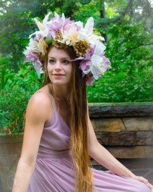 Person wearing floral crown and mauve dress in garden setting.