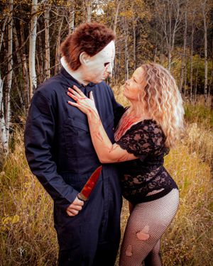 Dramatic Halloween-themed couple photoshoot in autumn woods with figure in Michael Myers costume and black lace outfit.