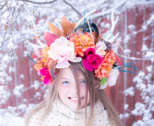 Winter portrait featuring vibrant coral and pink floral crown against snowy background.