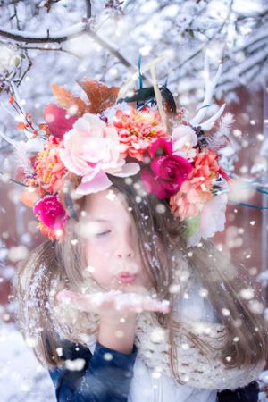 Dreamy winter portrait with person blowing snow while wearing bright floral crown.