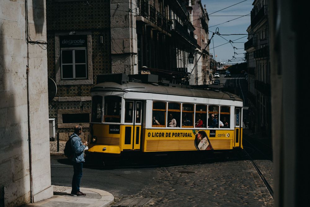 Yellow tram moving through narrow cobblestone street in historic city center.