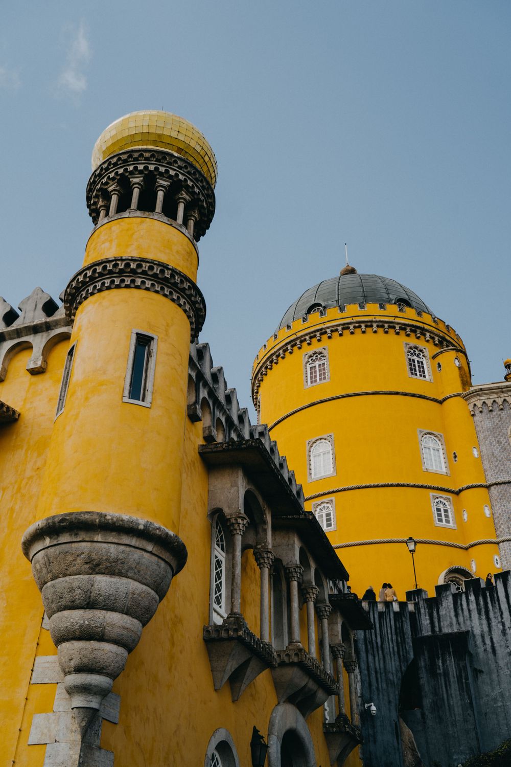 Yellow castle towers with ornate architectural details rise against a bright blue sky.