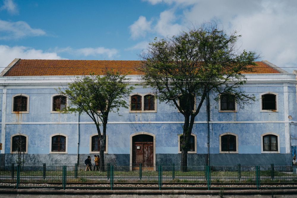 Row of white colonial buildings with blue walls and arched windows along a rural road.