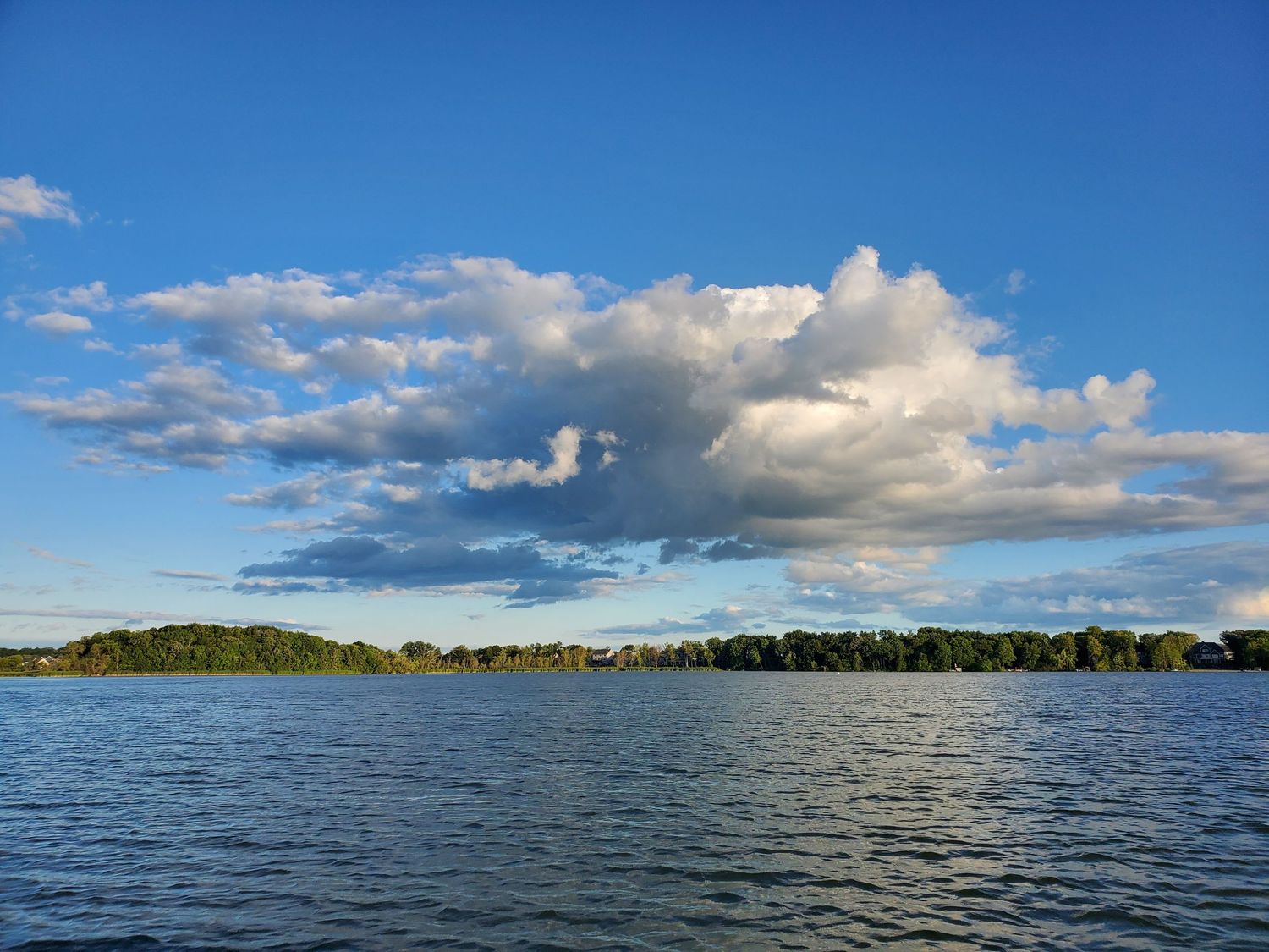 Dramatic clouds float over a serene lake landscape under bright blue skies.