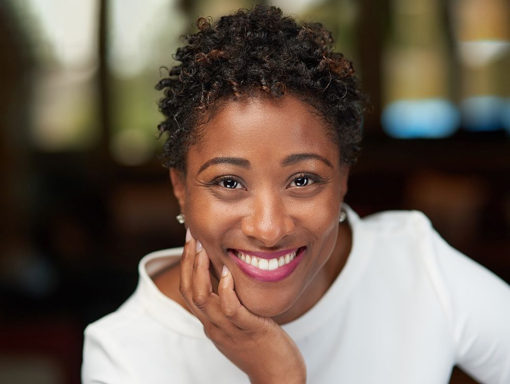 Smiling woman in white top resting chin on hand in warm candid close-up portrait.