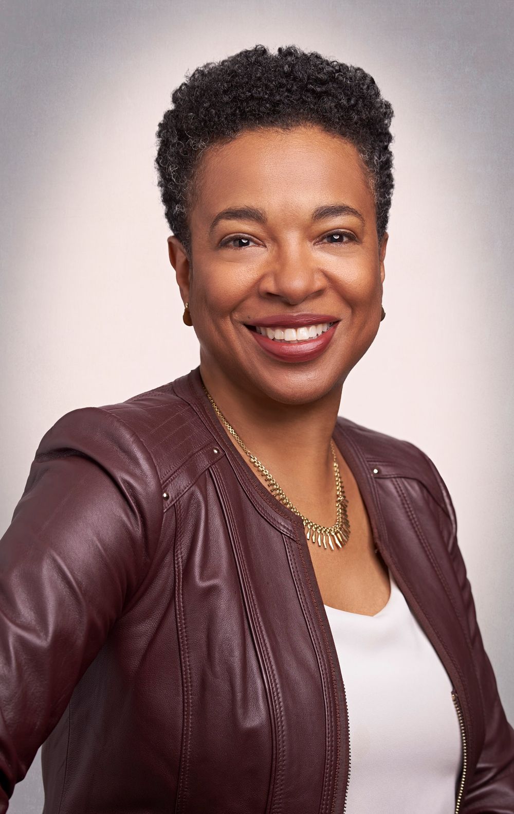 Smiling woman in burgundy leather jacket and gold necklace in professional headshot.