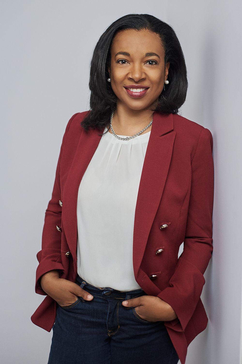 Professional woman in red blazer and white blouse poses against light gray background.