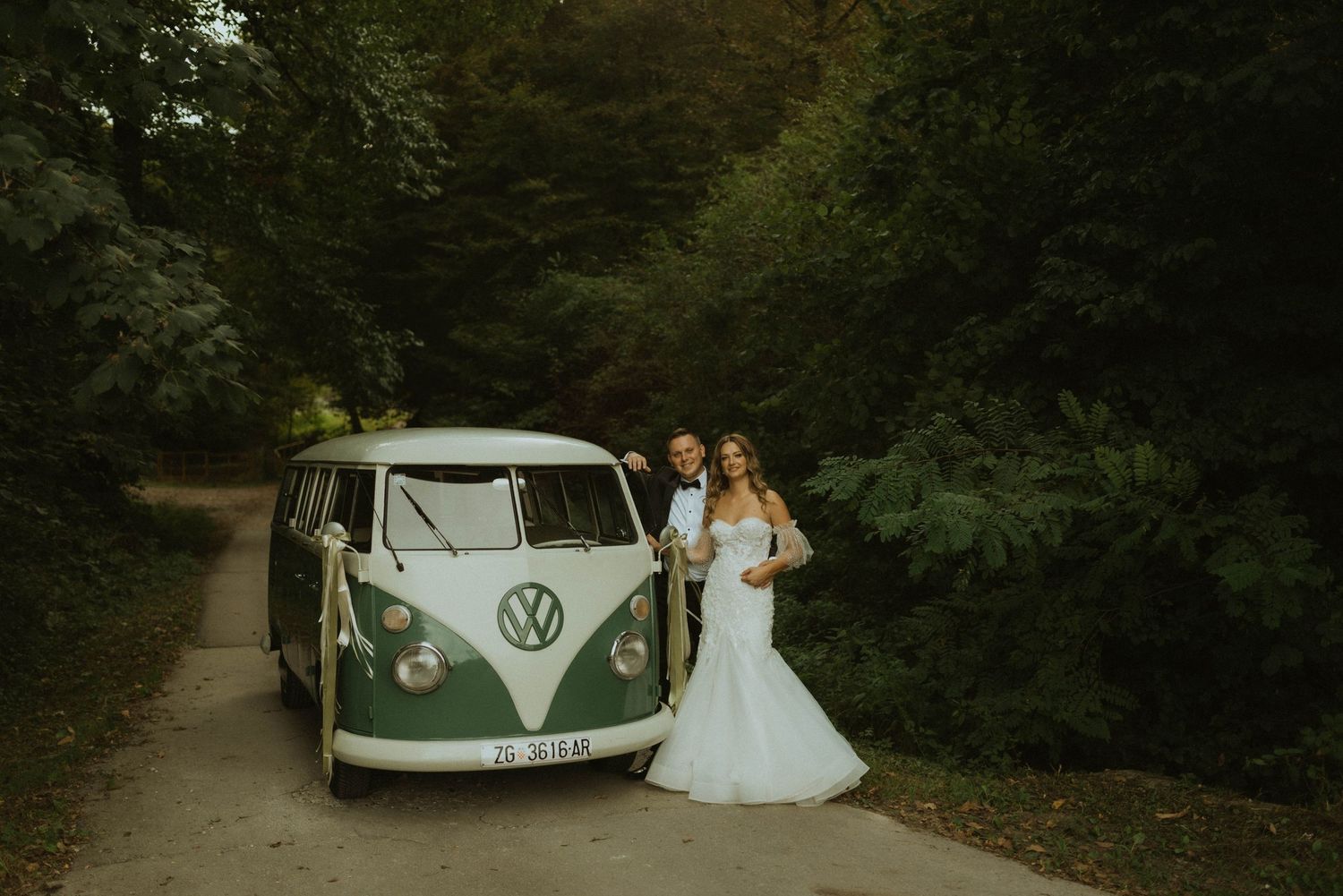 A couple poses with a classic VW van in a romantic forest setting.