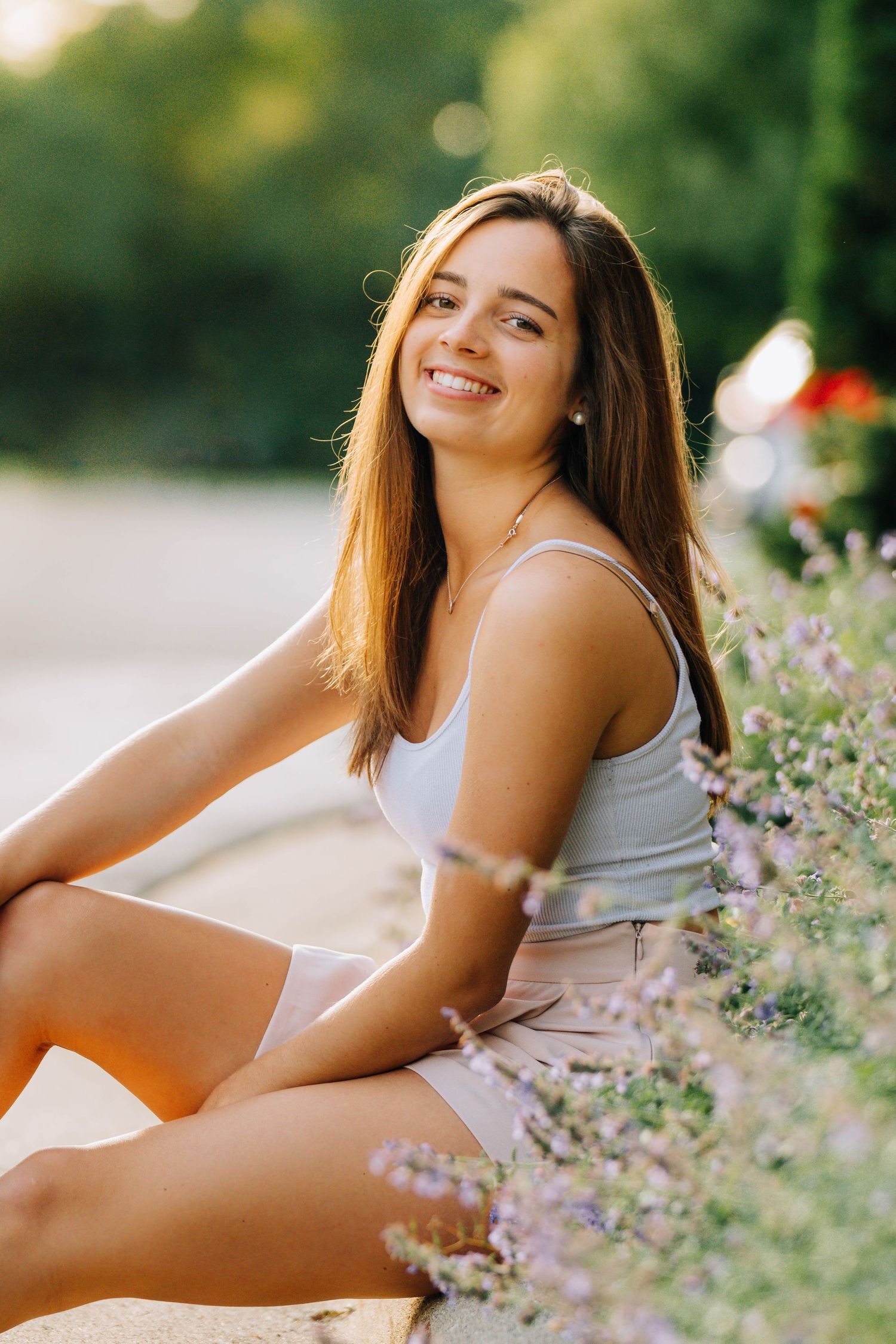 Person in white tank top lying in field of purple wildflowers at sunset.