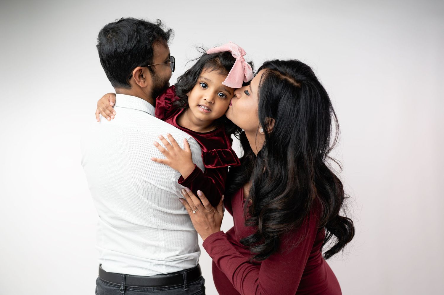 Professional maternity photo session showing tender family moments against white backdrop.