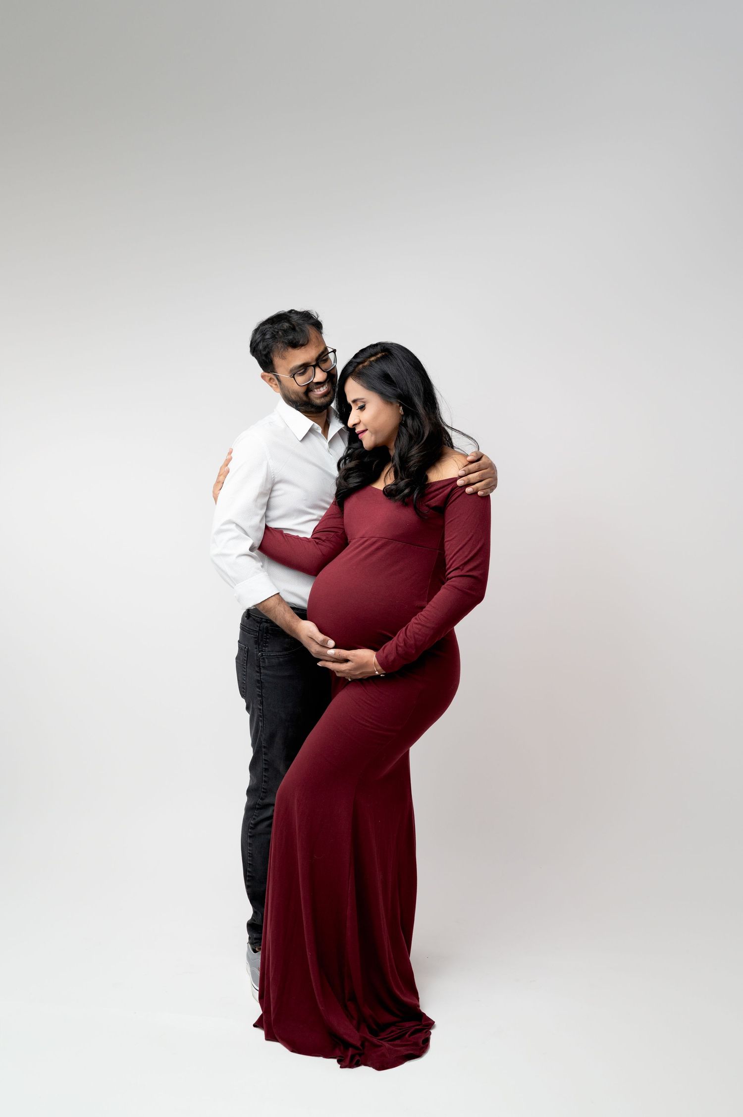 Couple embracing during maternity photoshoot against minimalist white background.