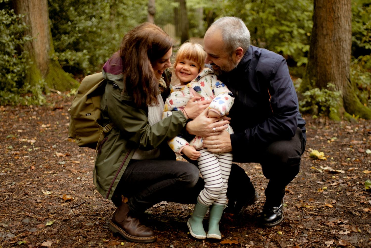 Natural family portrait in the woods, happy toddler smiling in the centre