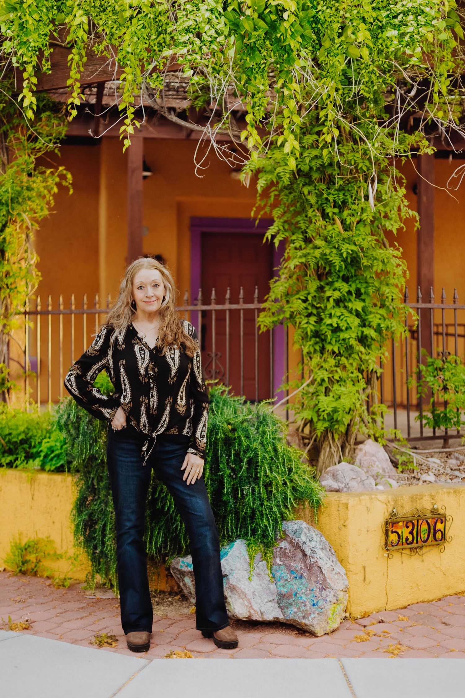 Fashion portrait against terracotta wall with hanging vines and purple door in desert setting.