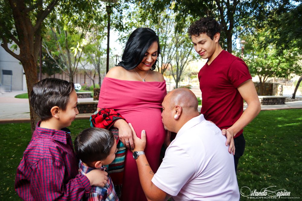 A joyful family maternity photo shoot in a park with children gathered around.