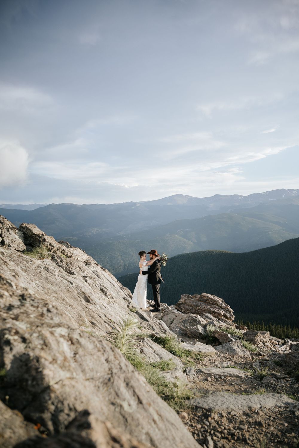 bride and groom holding each other kissing on rocky mountaintop view