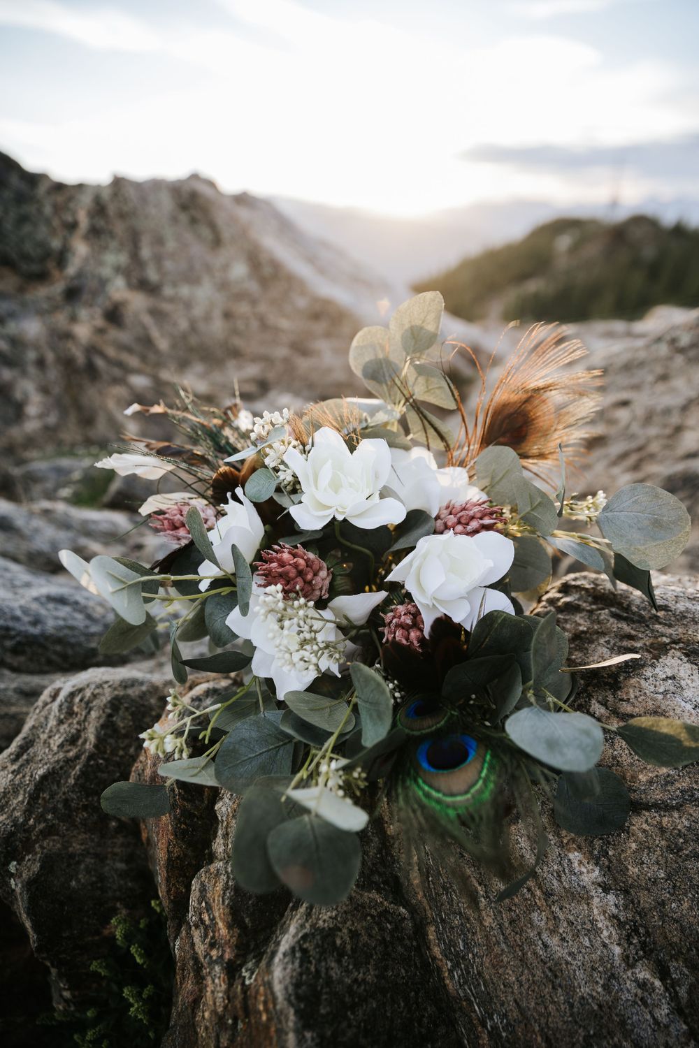 wedding bouquet with eucalyptus white roses feathers on rocks mountaintop sunset