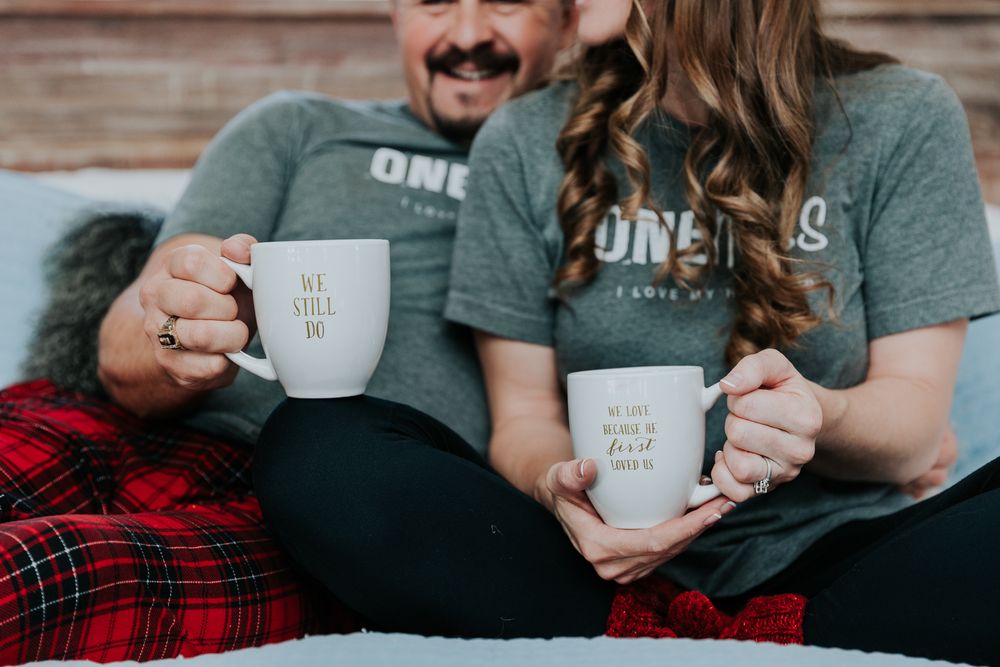 coffee mugs being held by anniversary couple husband man wife woman in pajamas on bed