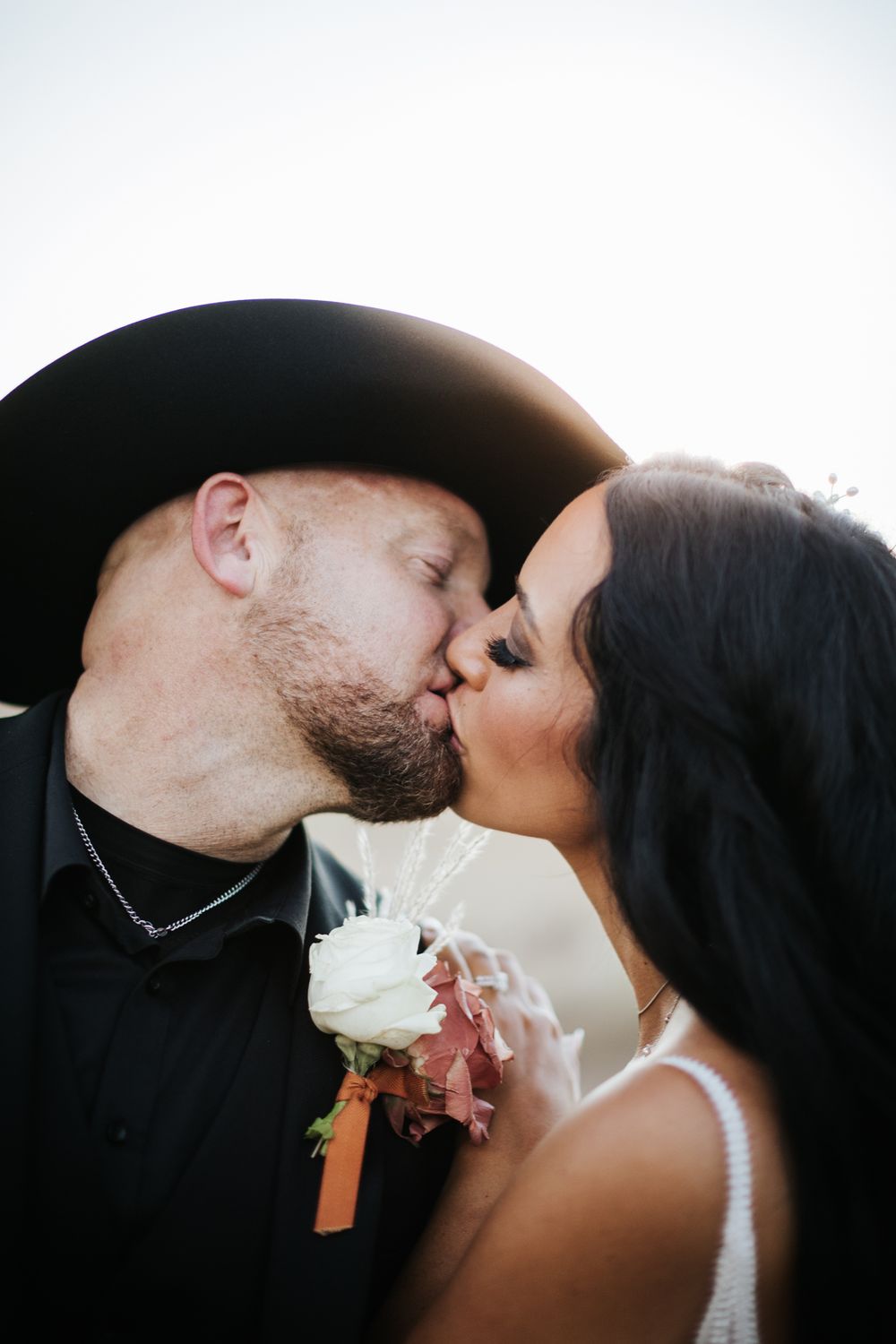 bride in white lace dress groom in black suit with black cowboy hat kissing