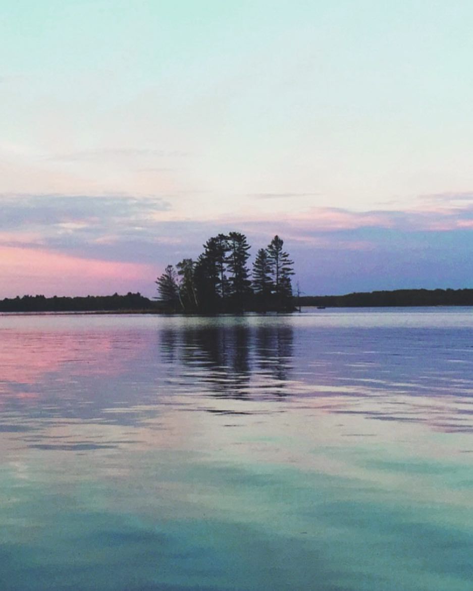 Serene lake landscape at sunset with small islands and trees silhouetted against pastel sky.