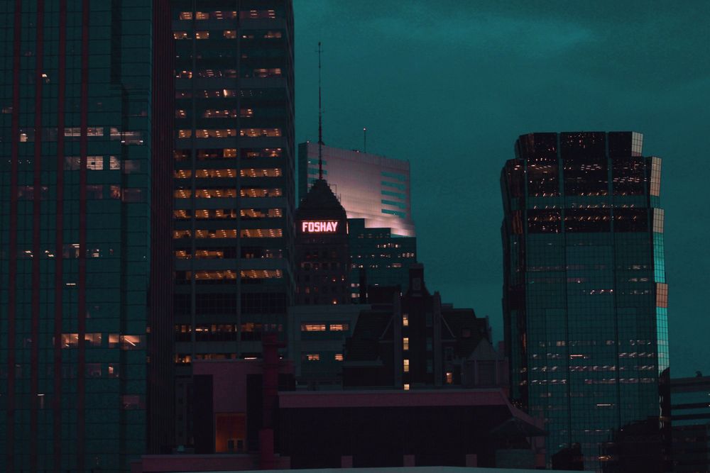 City skyline at dusk with illuminated office buildings against teal sky.
