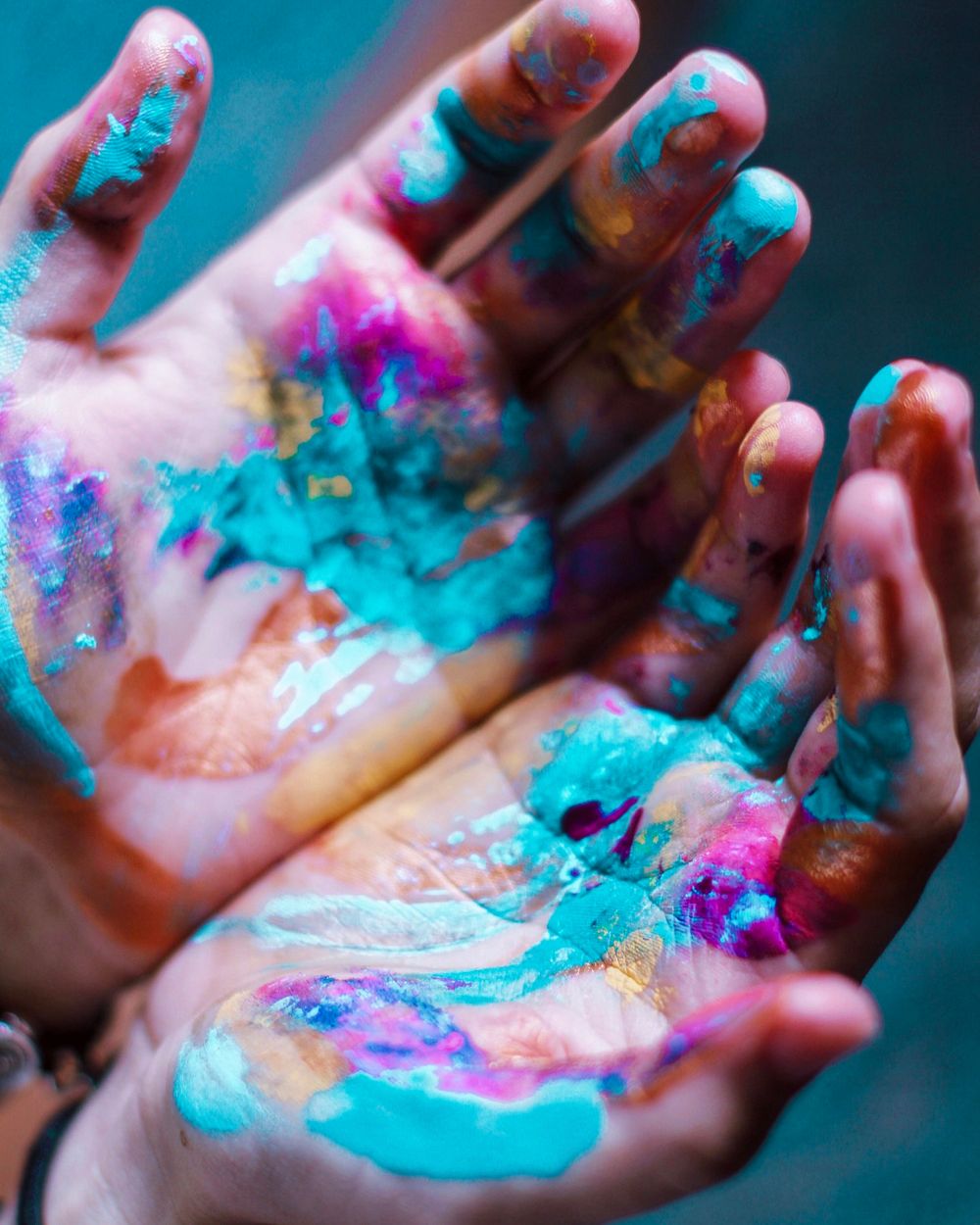 Hands covered in vibrant turquoise and pink powder paint creating an artistic display.