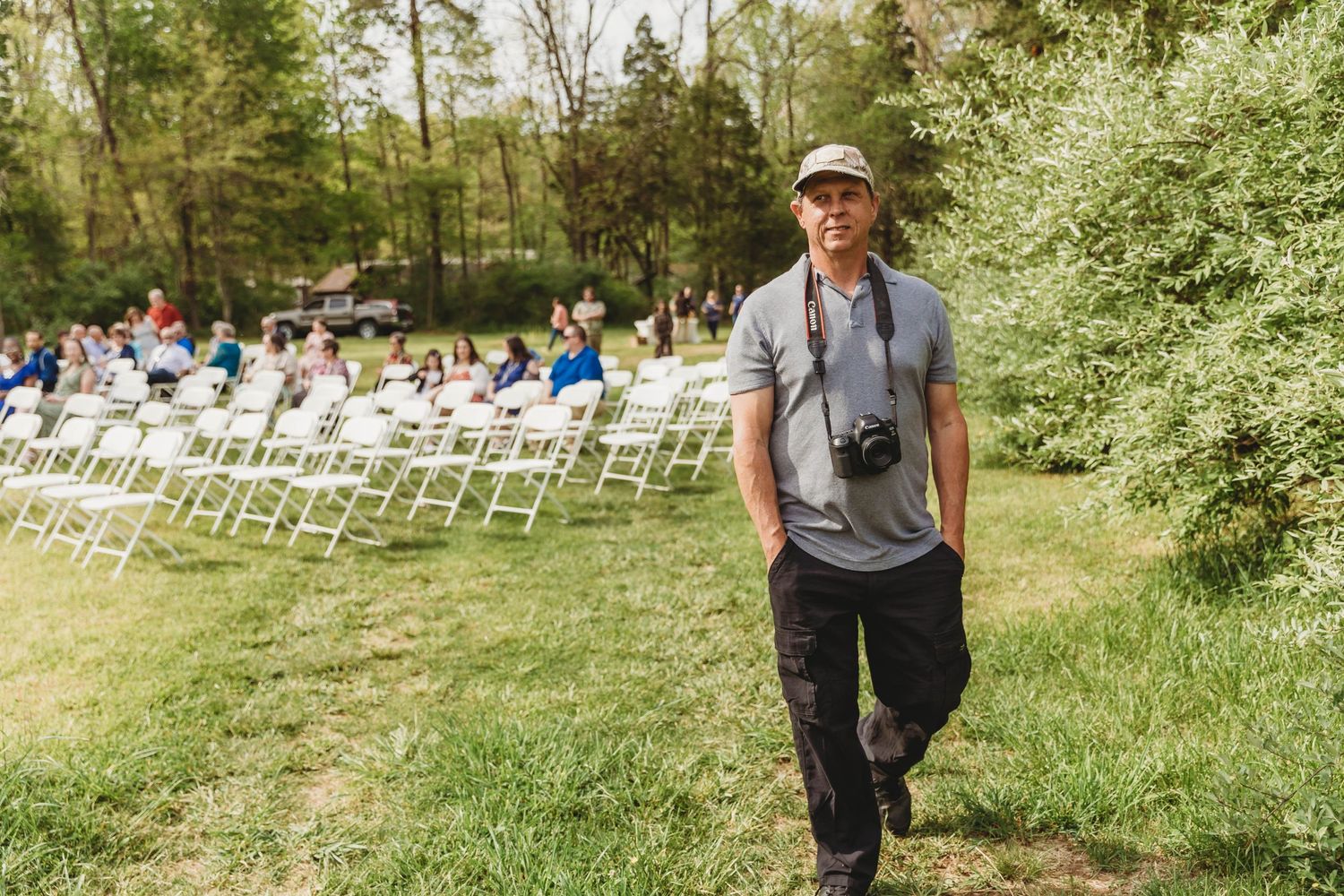 Wedding photographer with camera stands near rows of white chairs set up outdoors.