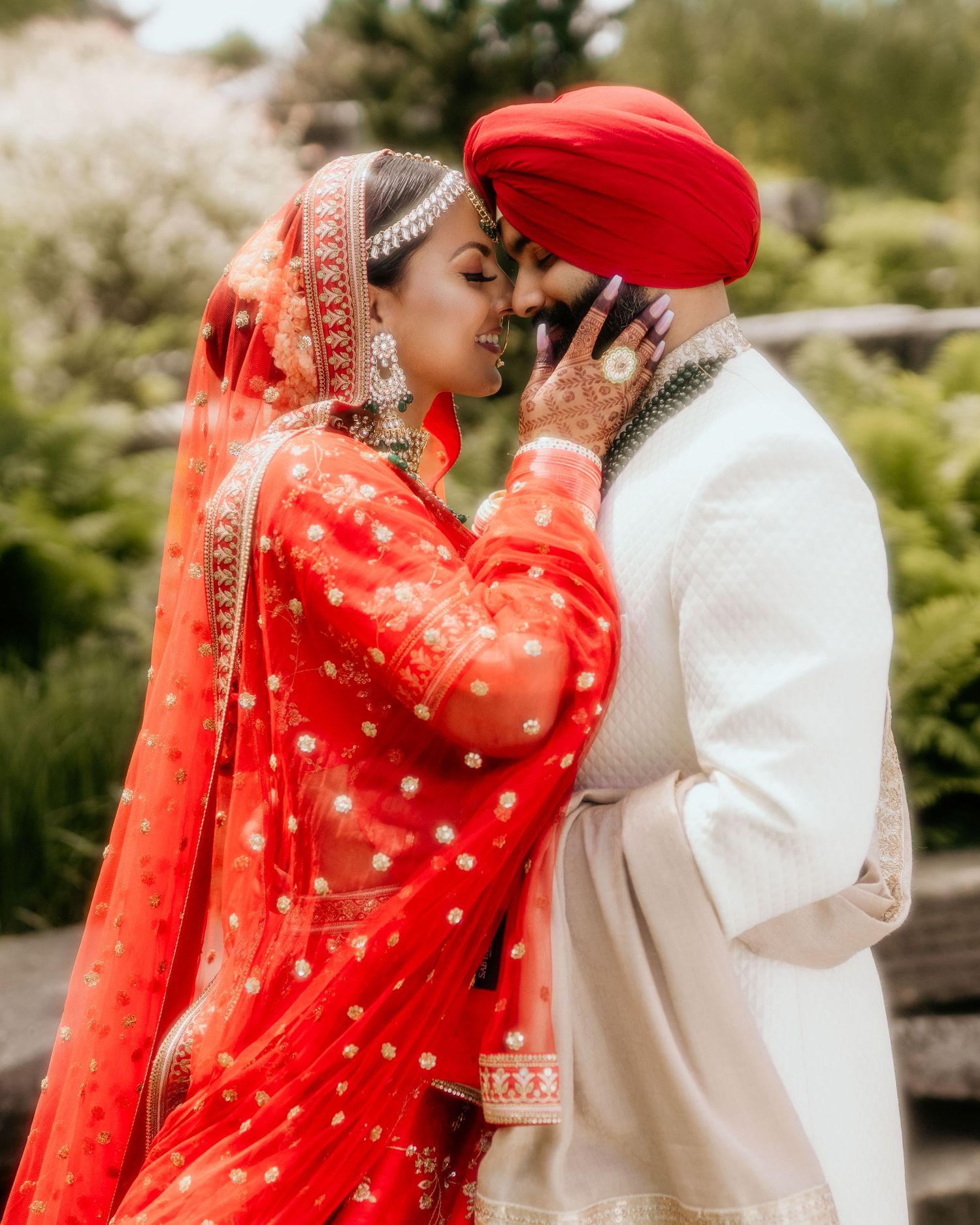 A traditional Sikh wedding couple in red and white attire share an intimate moment.