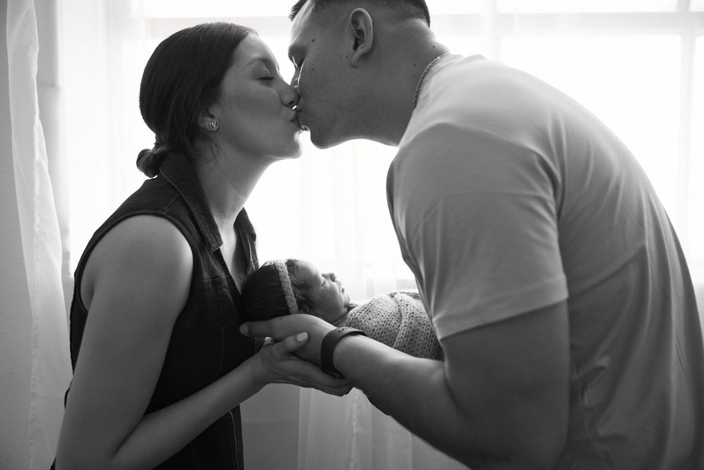 Intimate black and white portrait of new parents sharing tender moment with newborn.