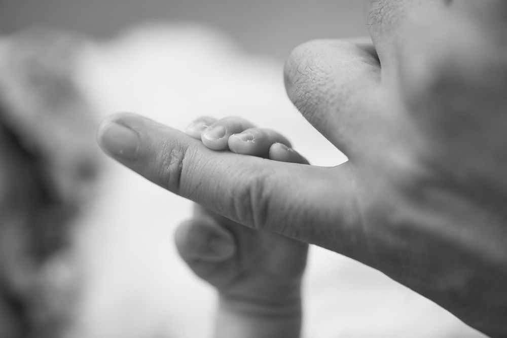 Close up of hands holding a delicate white wedding dress fabric against a blurred background.