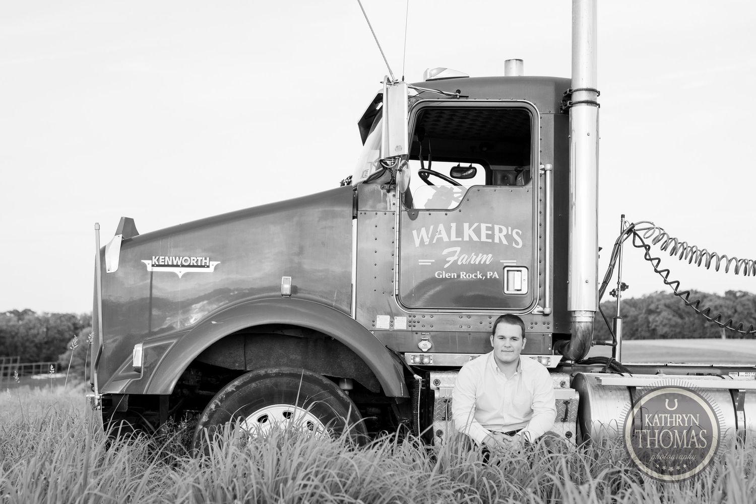 Black and white portrait of trucker beside Walker's Farm semi truck in field.