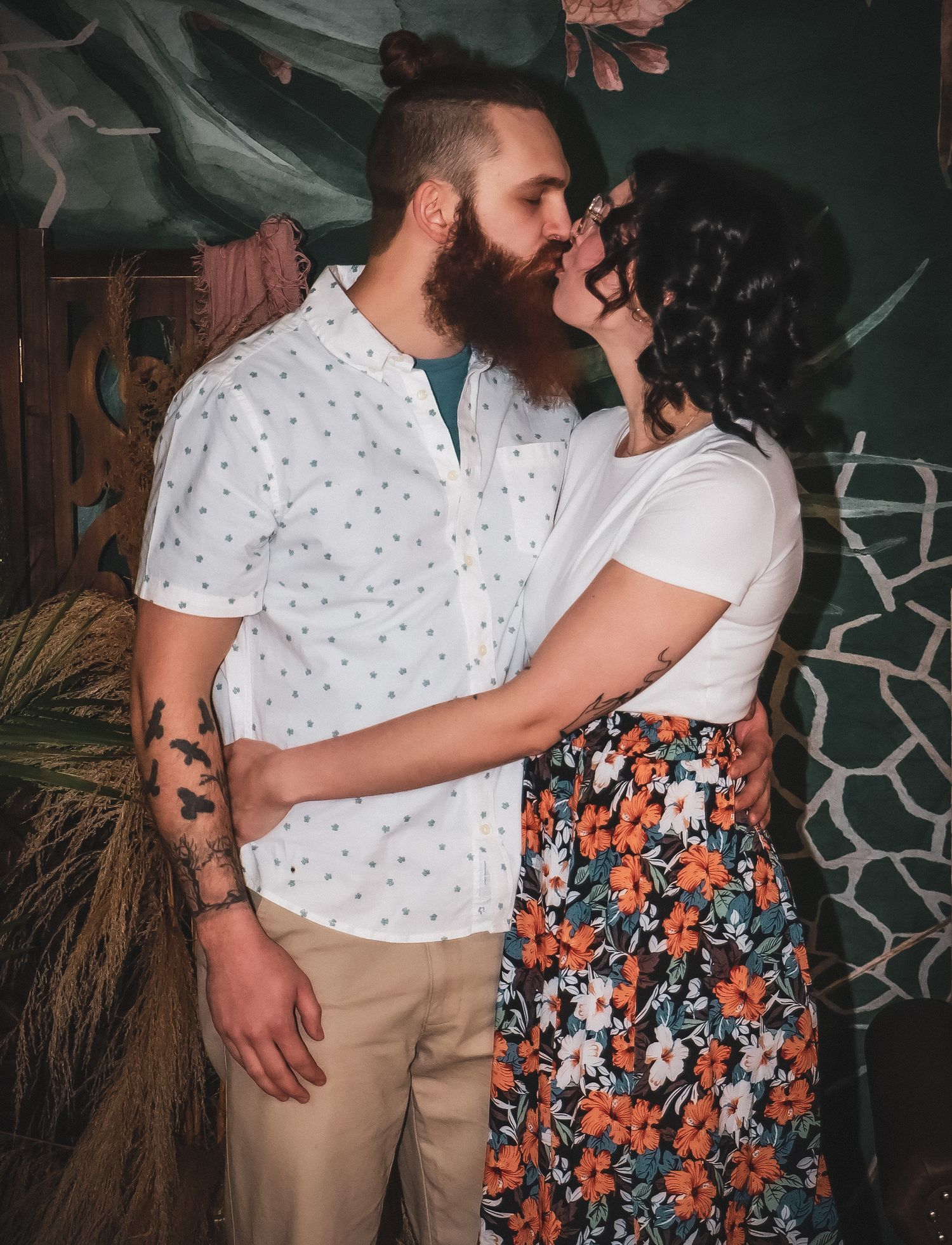 Romantic couple poses against a dark tropical backdrop with decorative elements.