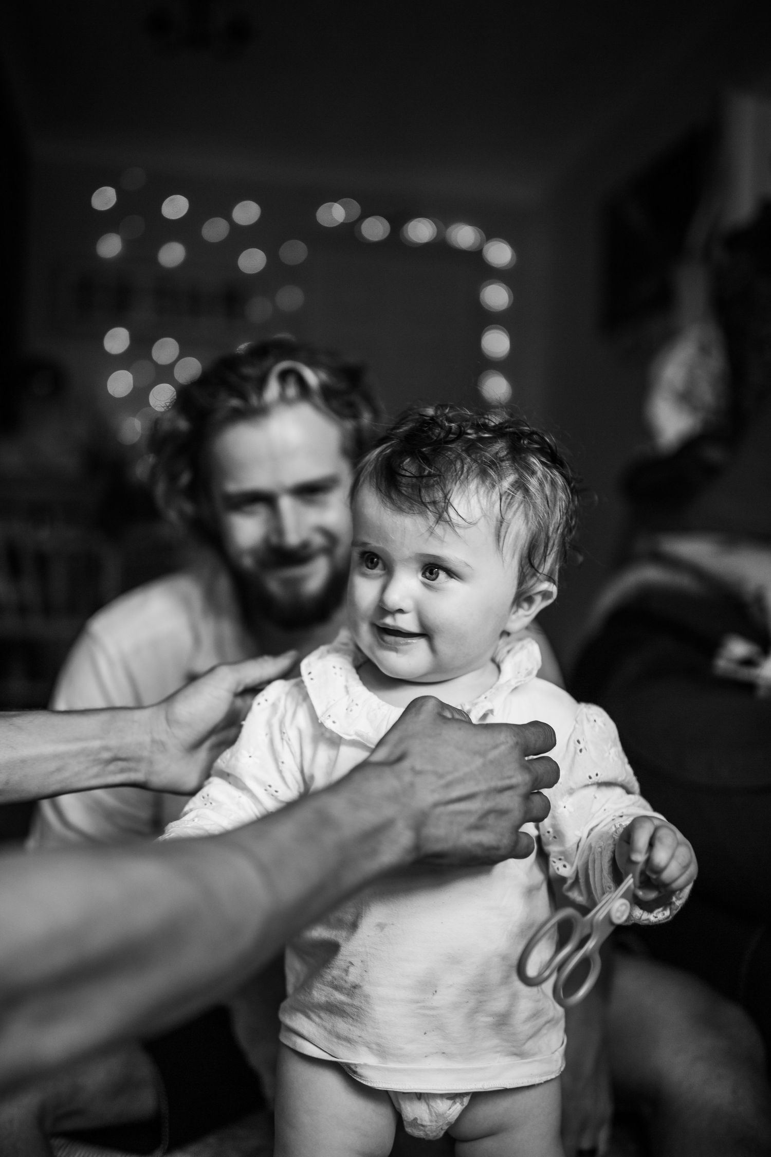 Black and white candid family moment with twinkling lights in the background.