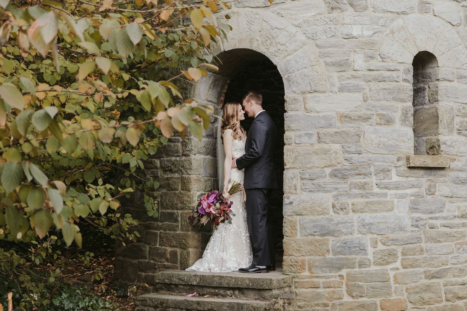 Wedding couple posing romantically against stone castle wall.