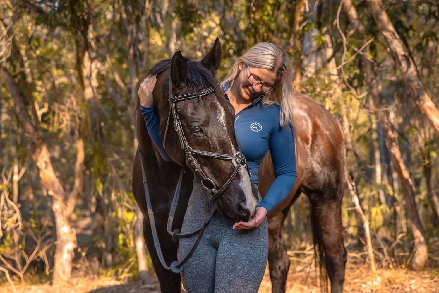 A girl holds her horses head in her hand while feeding him a treat