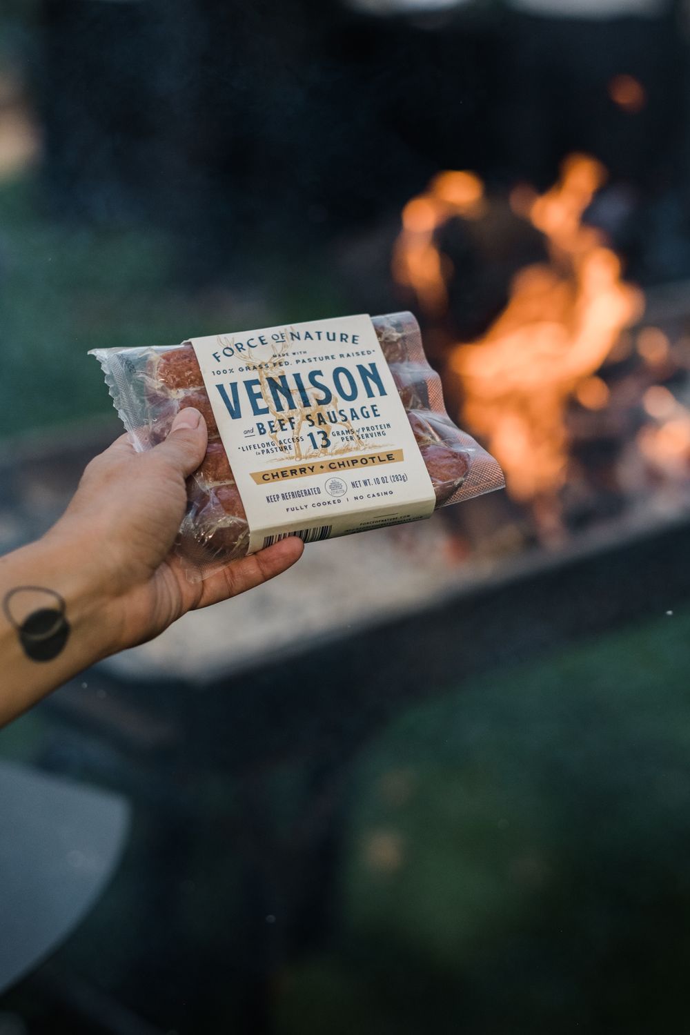 Venison meat snack packages held up against a campfire background.