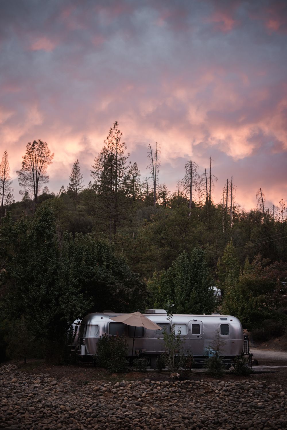 Row of silver Airstream trailers parked under a dramatic sunset sky.