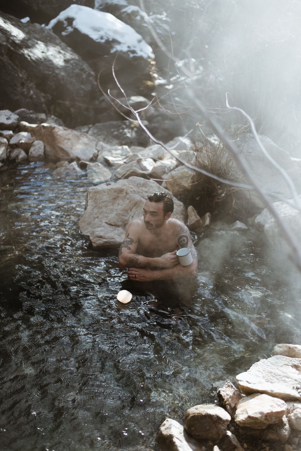 Someone soaking in misty natural hot springs surrounded by rocky terrain.