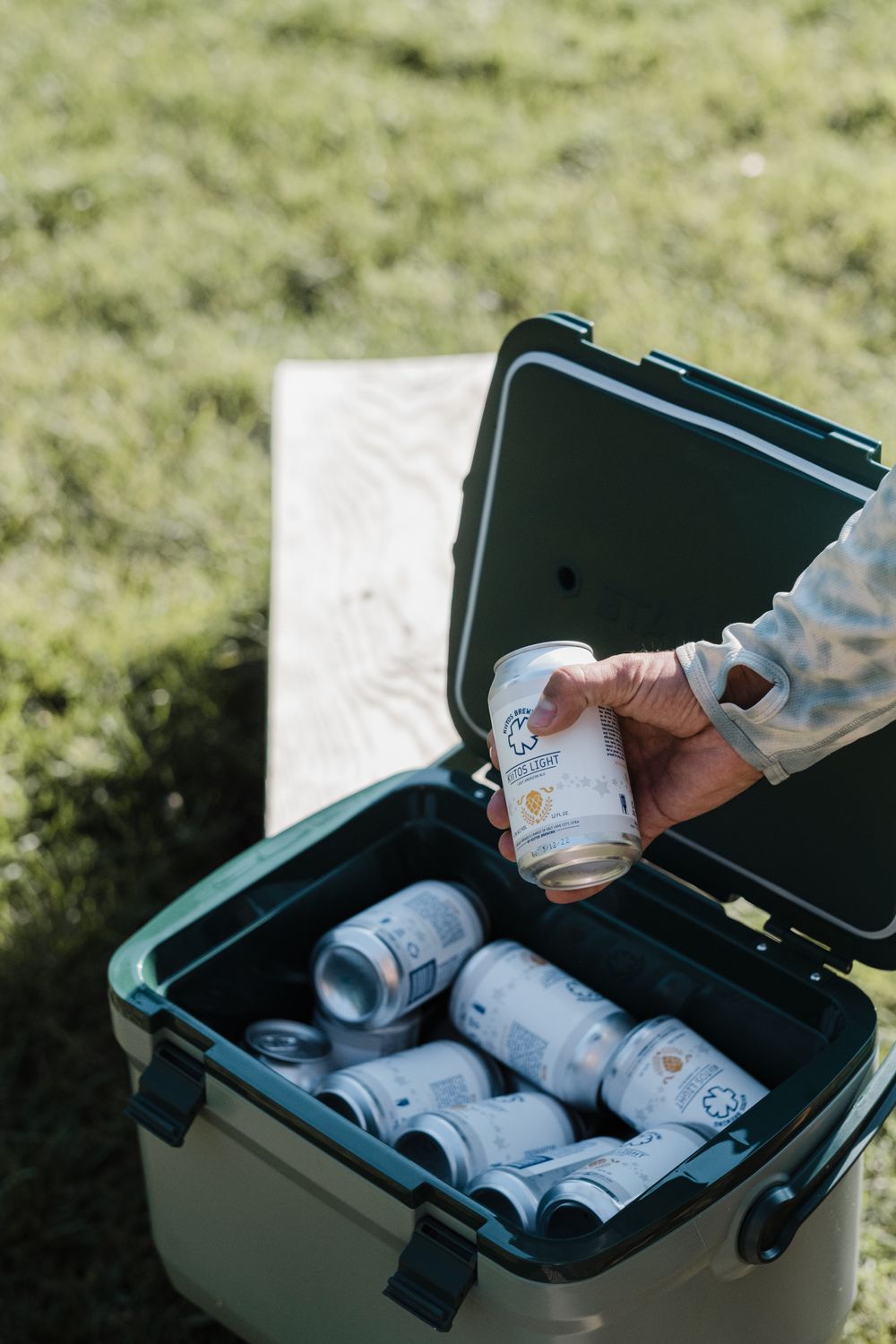 White canned beverages stored in an open green cooler on grass.