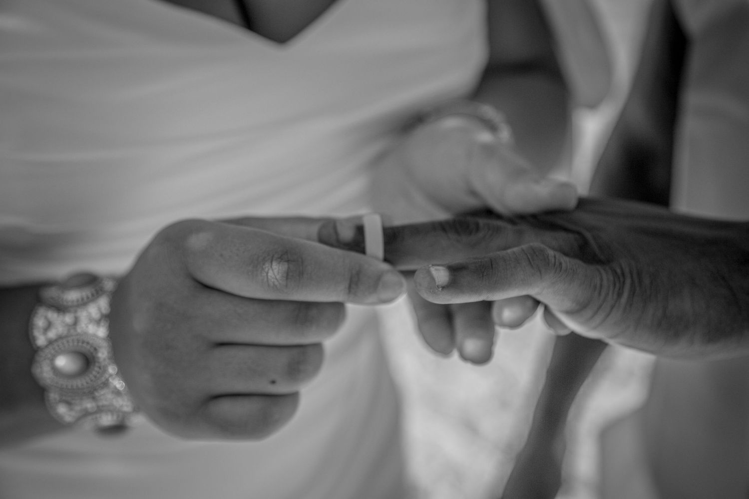 Black and white close-up photo of wedding ring exchange between hands.