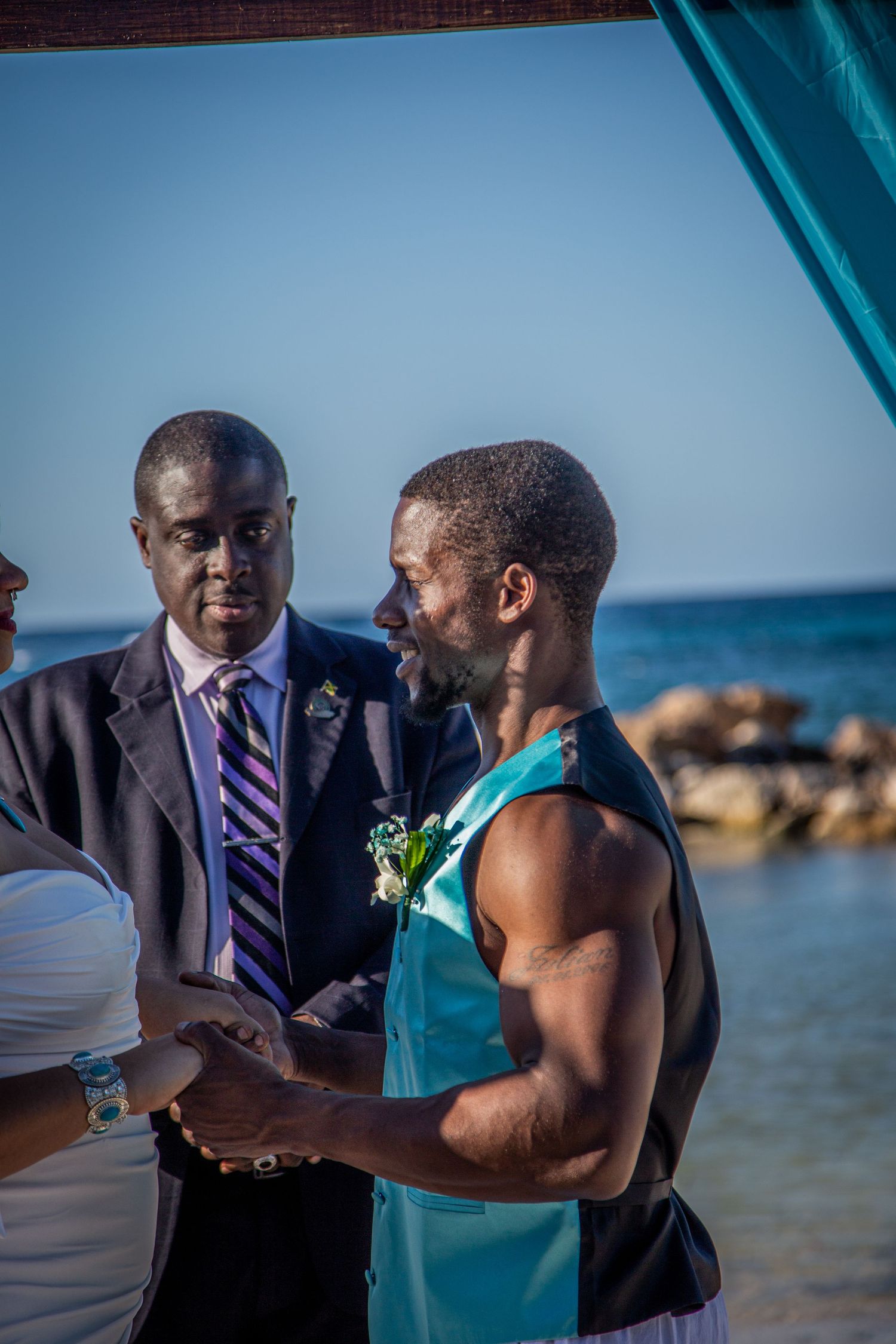 Wedding officiant and participants exchanging vows during beach ceremony under blue skies.