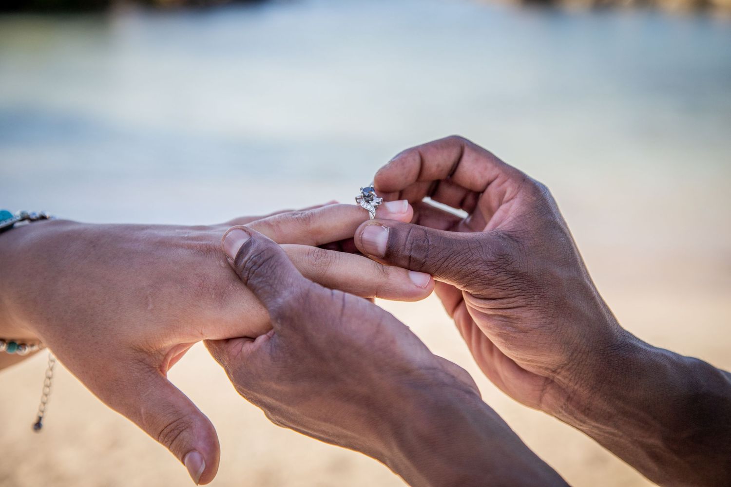 Close-up of hands exchanging wedding rings during beach ceremony.