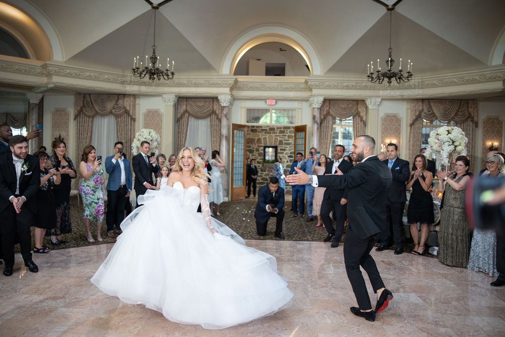 Wedding couple performs choreographed dance in grand ballroom as guests watch from sides.