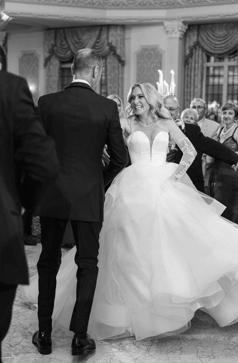 Wedding dance captured in black and white showing movement of elegant ball gown in ornate venue.