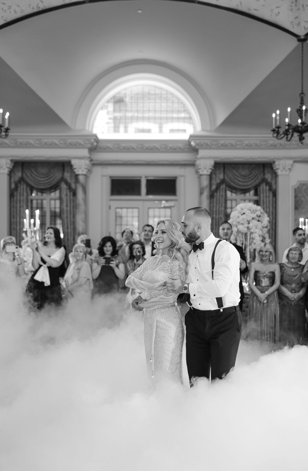 First dance moment with dramatic fog effect in elegant ballroom surrounded by guests.