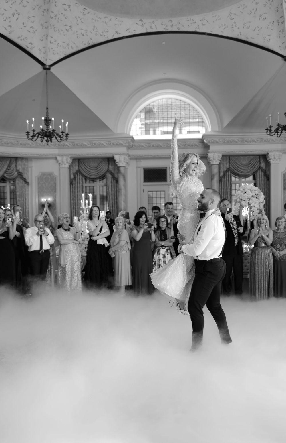 Dance performance in ornate ballroom with dramatic low-lying fog effect and chandeliers above.