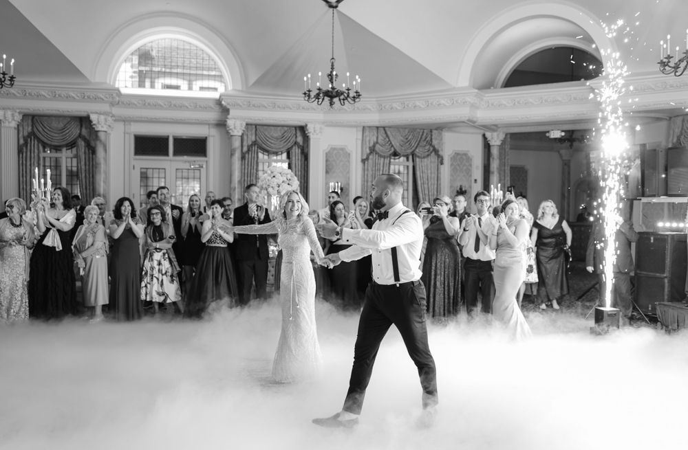 Black and white photo of wedding guests dancing in a ballroom filled with dramatic fog.