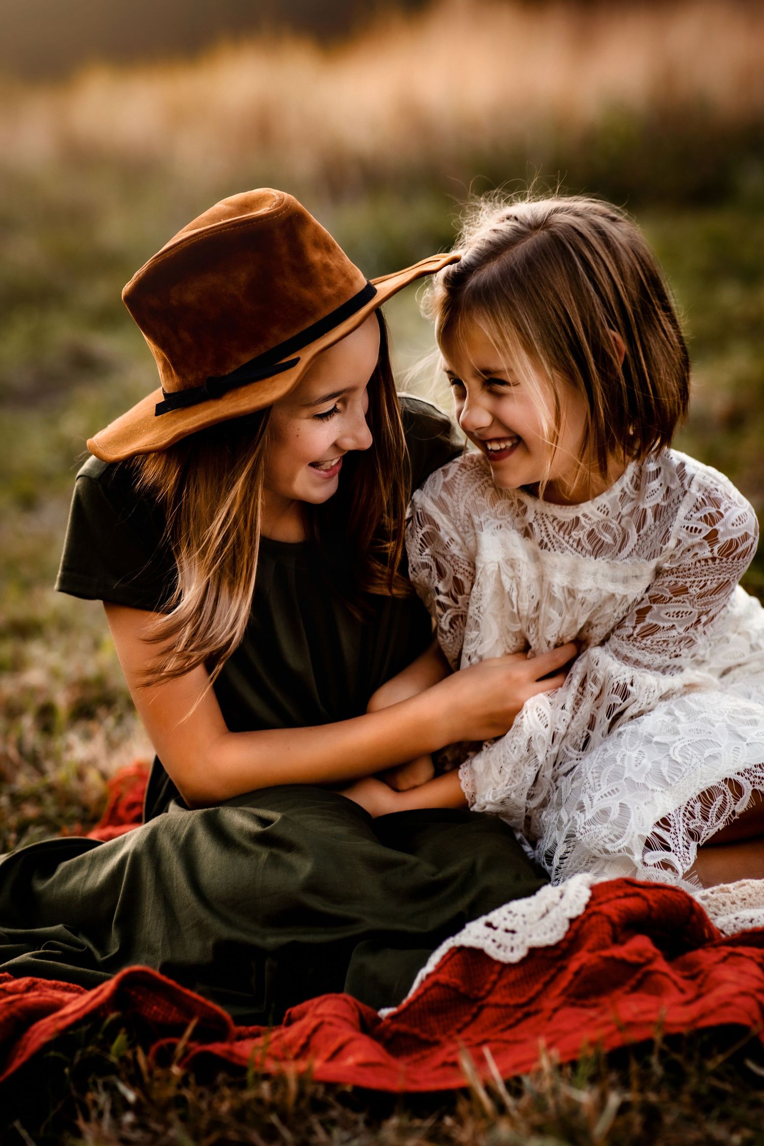 Two people sharing laughter while sitting on a red blanket in nature.