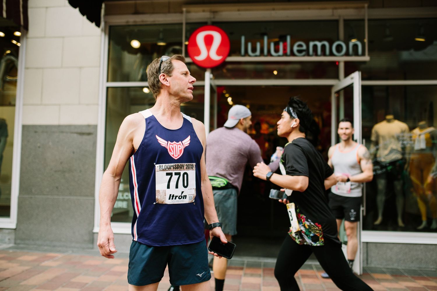 Male runner with bib number 770 running past a Lululemon store during a street race.