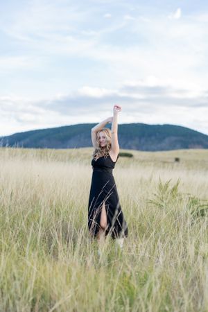 Dancing in a black dress through tall grass with mountains in the background.
